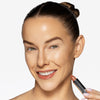 Model holding a terracotta lipstick in one hand, with the shade applied to her lips, showcasing a nude makeup look