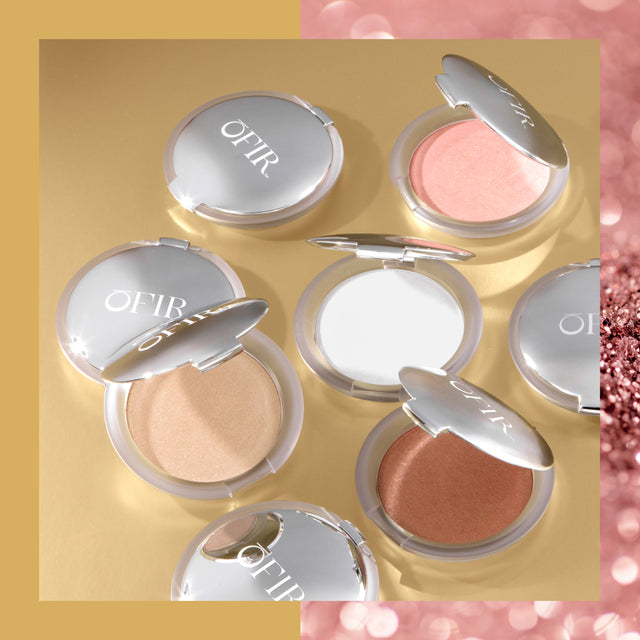 A collection of compact powders in various shades with silver lids, arranged on a gold and pink-toned background.