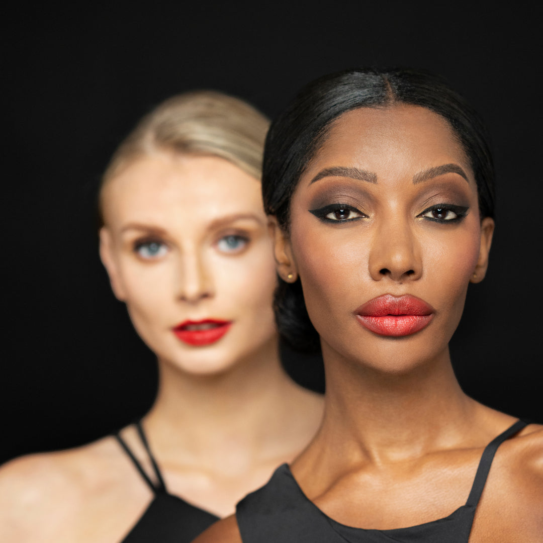 Two women with elegant makeup and red lipstick, showcasing beauty products against a dark background.
