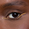 A close-up of an eye with striking gold eyeliner accentuating the eyelid, enhancing a bold makeup look.