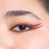 Close-up of a person's eye with intricate brown eyeliner featuring a double-winged design.