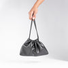 A hand holding a stylish, black drawstring pouch with a simple, elegant design against a neutral background.