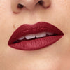 Close-up of lips adorned with a deep, rich matte red lipstick, highlighting smooth skin texture and a subtle beauty mark.