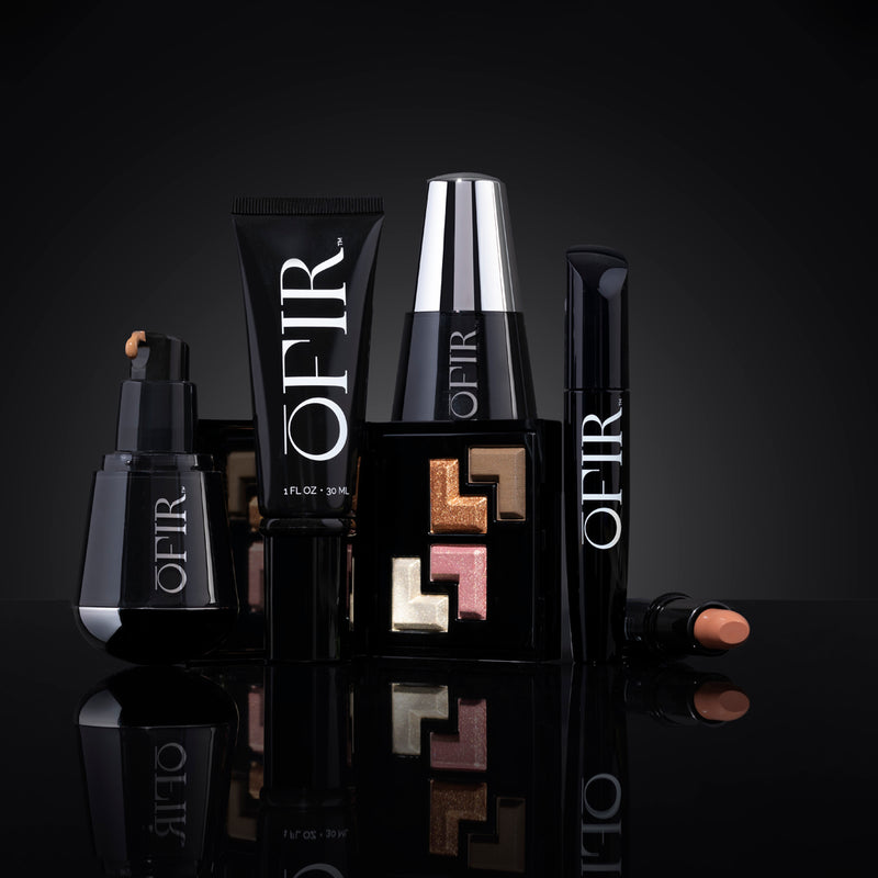Collection of luxurious OFIR beauty products, featuring a foundation, lipstick, mascara, and an eyeshadow palette with metallic shades, set against a sleek black background.