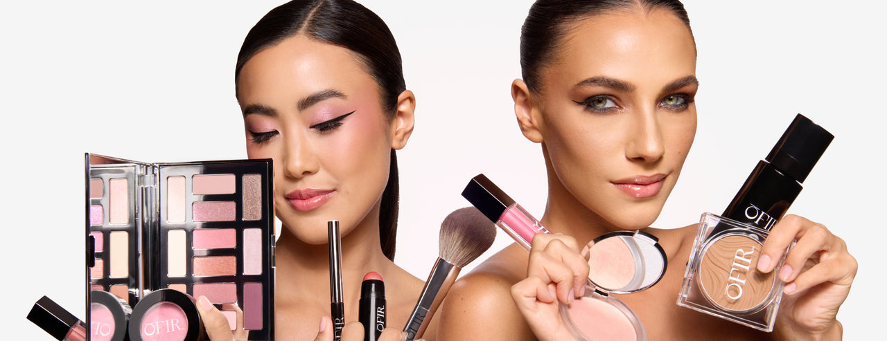 Two women posing with makeup products including eyeshadow palette, brushes, blush, lipstick, and highlighter