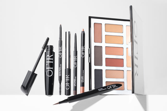 eye makeup products displayed on a white background, including a black mascara, brow liner, brow tonic, a eyeliner pencil and a nude tone pallet 