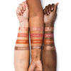 Three arms with different skin tones display swatches of makeup shades labeled Sunset Pearl, Red Earth, Summer Pop, and Dune Shimer.