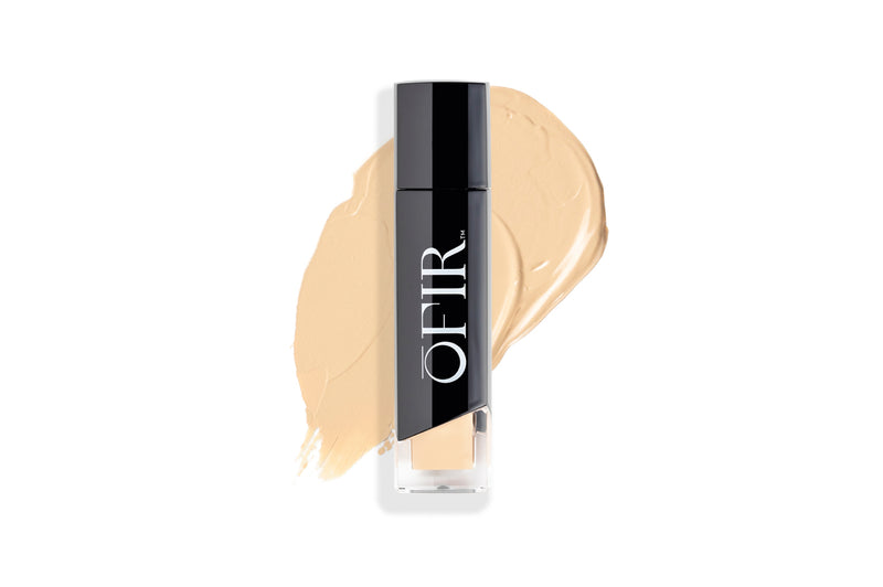 A foundation bottle with a sleek black cap is displayed against a backdrop of creamy beige makeup swatch.