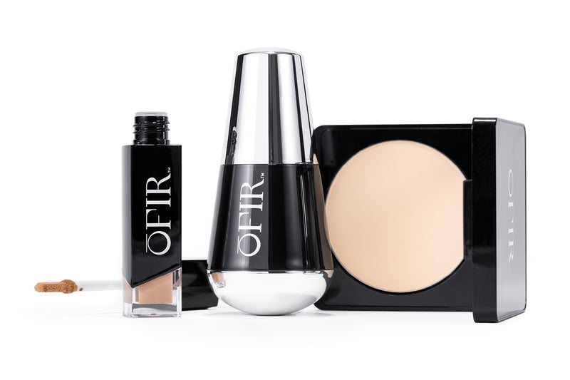 A set of OFIR beauty products featuring a liquid foundation with a doe-foot applicator, a sleek silver and black bottle, and a compact with light-colored pressed powder.