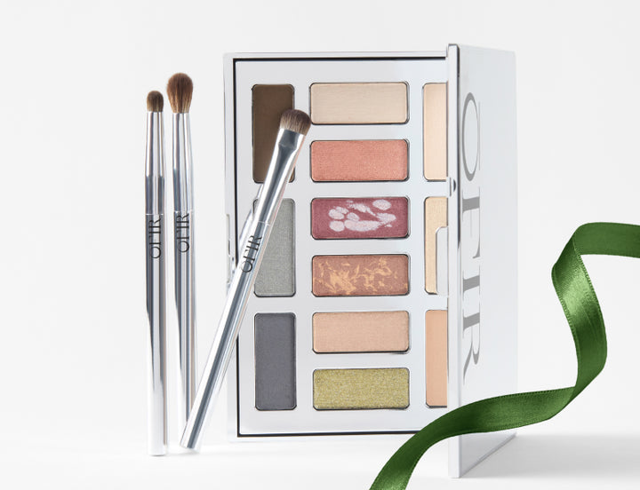 eyeshadow palette with brushes and green ribbon displayed on white surface