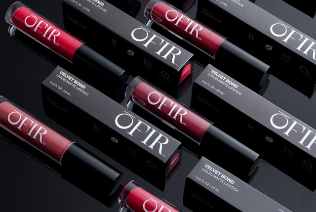 Several tubes of Velvet Bond liquid matte lipstick with bold branding are arranged alongside their sleek black packaging.