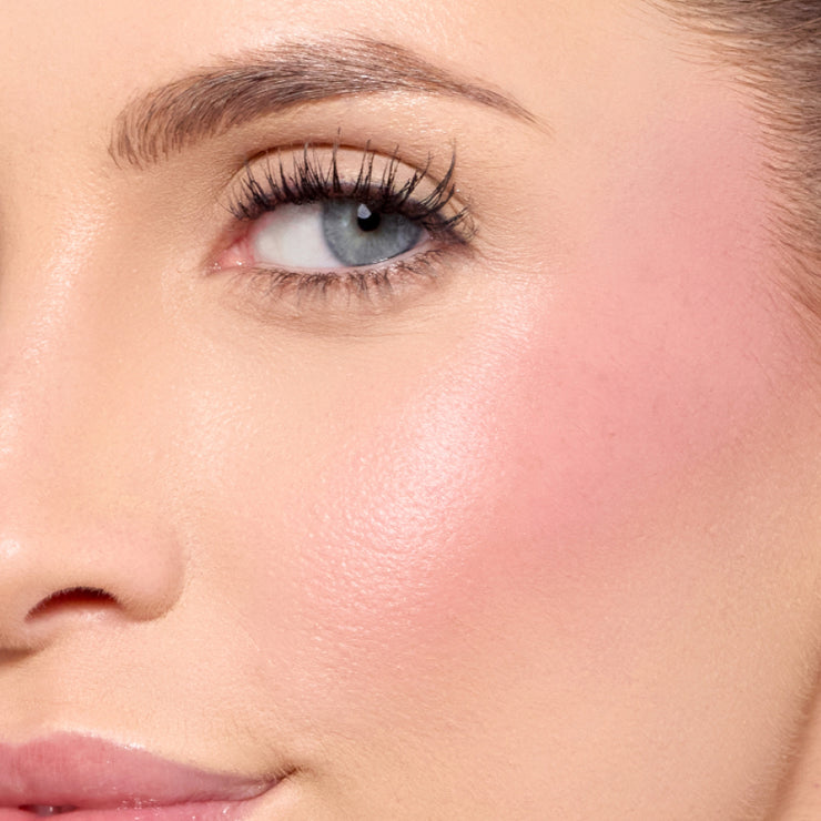 Close-up of a model’s cheek and eye area featuring a soft pink blush with a luminous finish