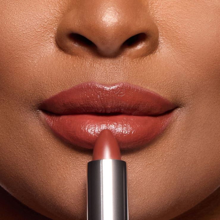 Close-up of a model applying a nude rose lipstick, showcasing full lips with a glossy finish and smooth