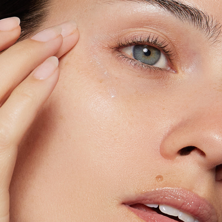 Close-up of a model’s eye and upper cheek with a dewy serum and a soft neutral shimmer, highlighting smooth texture and natural radiance