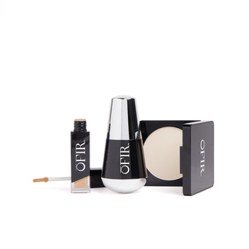 A collection of sleek black and silver beauty products including a concealer with an applicator, a cylindrical bottle, and a compact with powder.