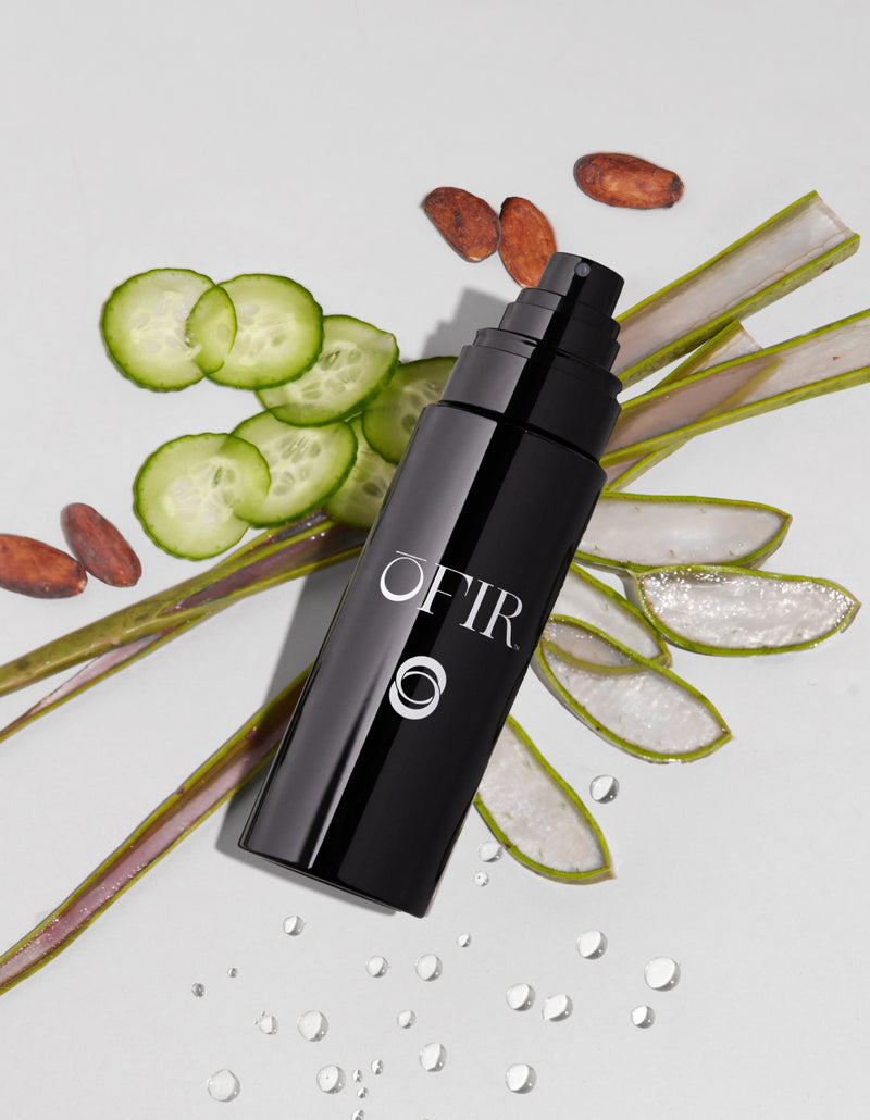 A sleek black bottle labeled "OFIR" is surrounded by fresh cucumber slices, aloe vera leaves, seeds, and water droplets, suggesting a refreshing and natural essence.